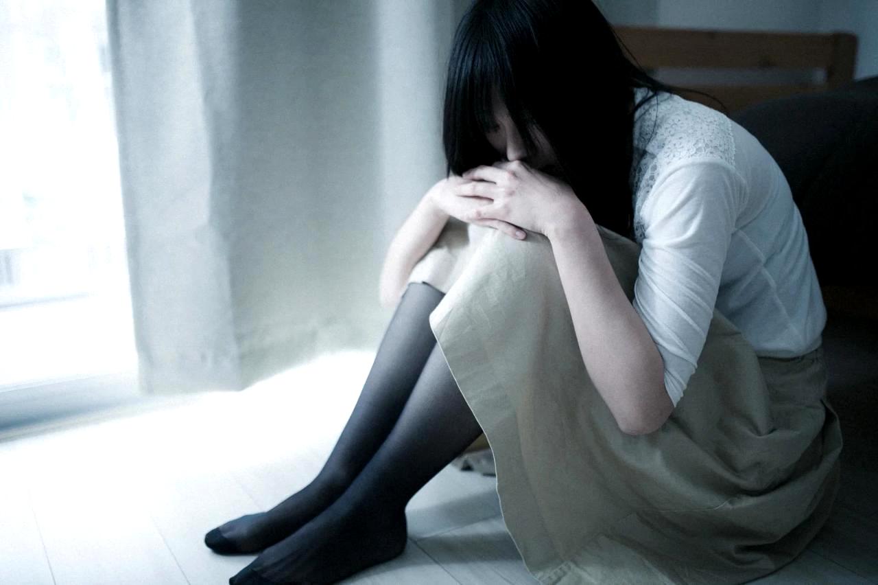 女性が窓の外を見つめて元カレとの思い出に悩んでいる様子、復縁の心理を整理する