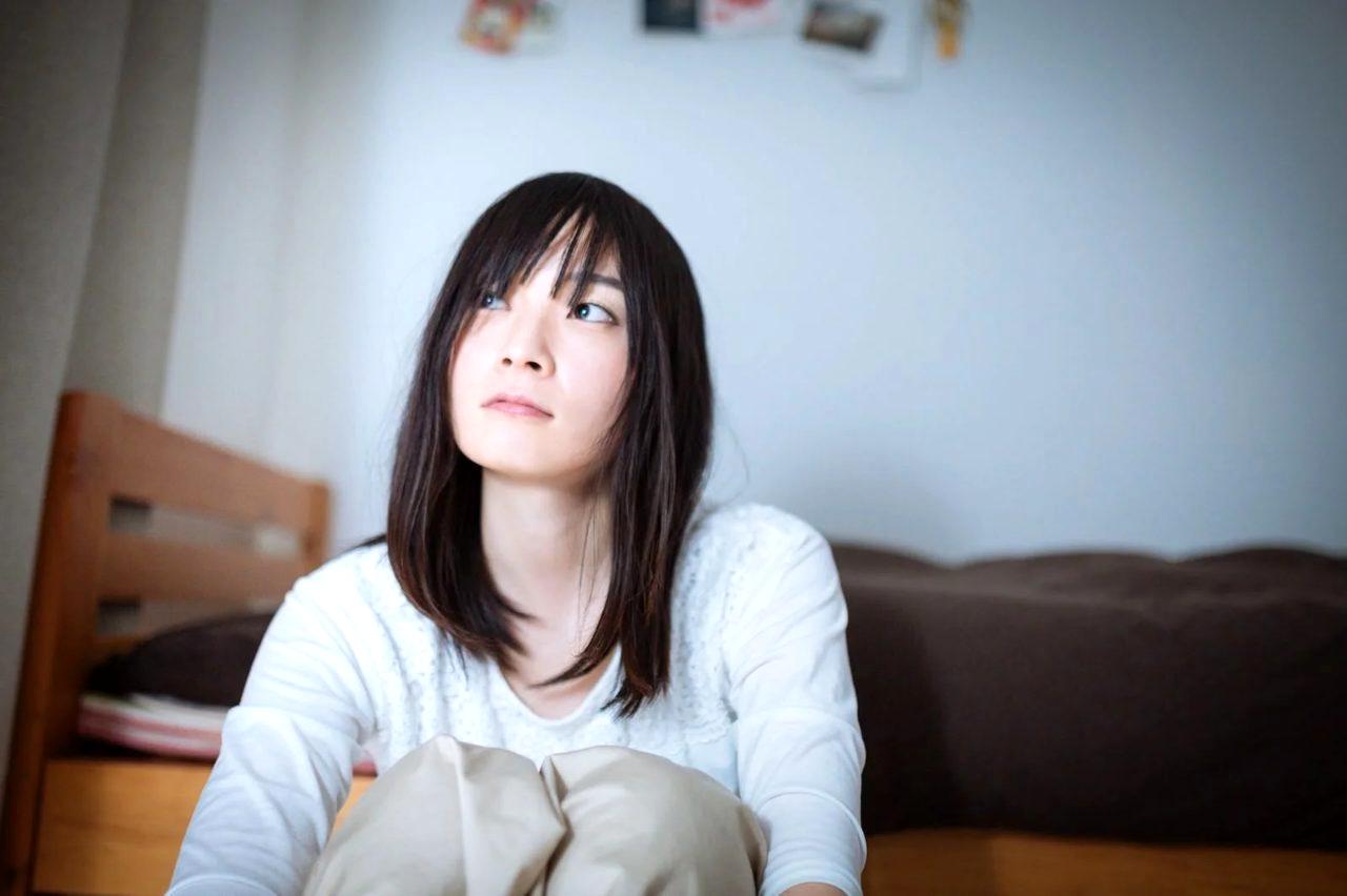 ベッドに座り込み顔を覆う女性。罪悪感に苦しむ夜の静かな部屋の様子