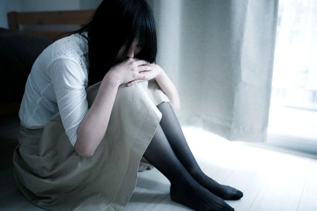 一人で悩む女性の後ろ姿、職場の窓から差し込む光