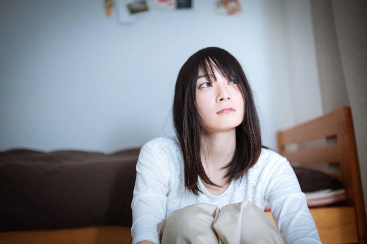 毛布にくるまり静かに心を休めている、疲れた表情の女性のイメージ